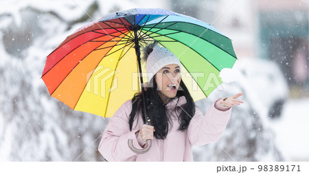 Happy woman holding an umbrella on a cold snowy day and throwing fresh snow Happy woman holding an umbrella on a cold snowy day and throwing fresh snow 98389171