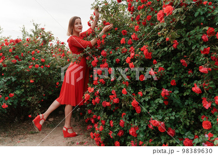 Portrait of a beautiful blonde in a red dress in a garden with red roses 98389630