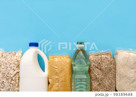 Food supply. Raw porridge, cereals, milk and vegetable oil on the blue table. Copy of space, flat. Food security for the poor Food supply. Raw porridge, cereals, milk and vegetable oil on the blue table. Copy of space, flat. Food security for the poor 98389688