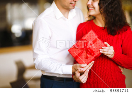 Man gives to his woman a gift box with red ribbon. A loving couple celebrating Valentine's Day. Man gives to his woman a gift box with red ribbon. A loving couple celebrating Valentine's Day. 98391711