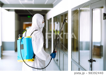 Contractor disinfecting office for COVID-19 coronavirus. A disinfector in a protective suit and mask Contractor disinfecting office for COVID-19 coronavirus. A disinfector in a protective suit and mask 98392440