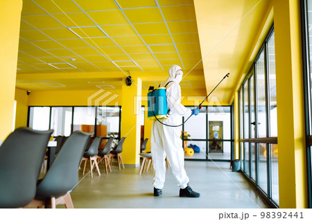 Contractor disinfecting office for COVID-19 coronavirus. A disinfector in a protective suit and mask Contractor disinfecting office for COVID-19 coronavirus. A disinfector in a protective suit and mask 98392441