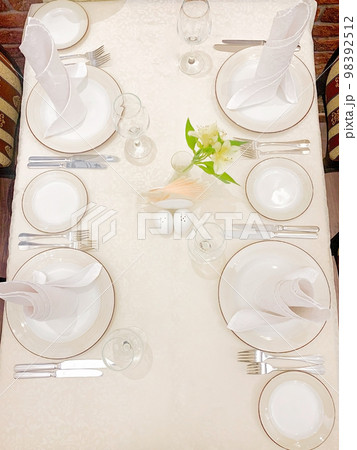 The dining table is covered with a white tablecloth, there are appliances on the table, plates on which there are waffle towels. Close-up view from above. High quality photo 98392512