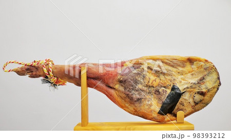 A front leg of Serrano ham mapped on a wooden stand on a white background. 98393212