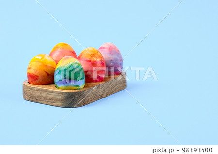 Colorful Easter eggs in a wooden egg stand on a blue background with a place for text. Happy Easter concept. Greeting card. 98393600