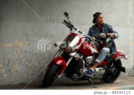 Handsome bearded biker with red motorcycle in classic style. Cafe racer in the garage. Handsome bearded biker with red motorcycle in classic style. Cafe racer in the garage. 98394115