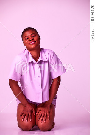 Overjoyed plus size millennial black woman in purple t-shirt and shorts sitting on floor relaxing isolated on purple studio background 98394120