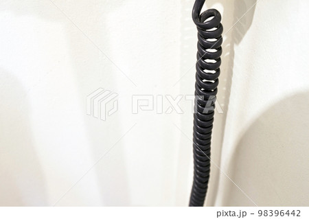 Spiral black spring telephone cable on white wall 98396442