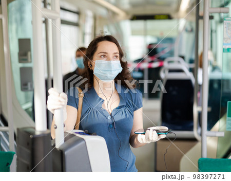Modern girl in protective medical mask and gloves traveling in tram and using mobile phone Modern girl in protective medical mask and gloves traveling in tram and using mobile phone 98397271