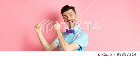 Image of cheerful man celebrating holiday, dancing and having fun, triumphing and saying yes with happy face, standing over pink background Image of cheerful man celebrating holiday, dancing and having fun, triumphing and saying yes with happy face, standing over pink background 98397314