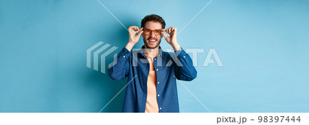 Happy caucasian man trying new glasses and smiling, standing on blue background 98397444