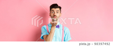 Cute boy sending air kiss at camera and saying I love you on Valentines day, standing over romantic pink background in bow-tie and shirt 98397492