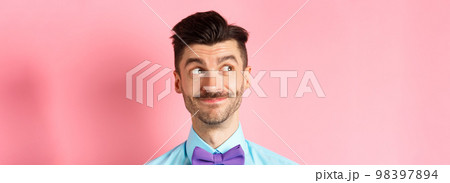 Close-up of handsome smiling guy with moustache, looking left at logo with pleased face, standing on pink background Close-up of handsome smiling guy with moustache, looking left at logo with pleased face, standing on pink background 98397894