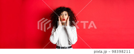 Surprised young woman hear amazing news, looking at promo and saying wow, stare with disbelief, standing on red background Surprised young woman hear amazing news, looking at promo and saying wow, stare with disbelief, standing on red background 98398211