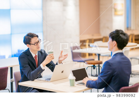 コーヒーを持って打ち合わせをするビジネスマン 98399092