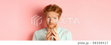Close up of funny bearded man with red hair pitching a perfect plan, smiling and steeple fingers, scheming something, standing devious against pink background 98399417
