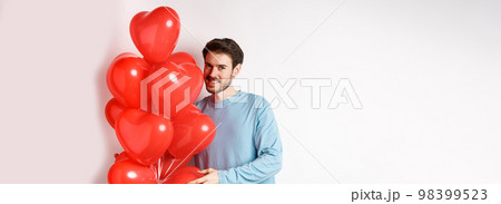 Romantic boyfriend bring red hearts balloons on Valentines day, surprise lover on date, standing over white background 98399523