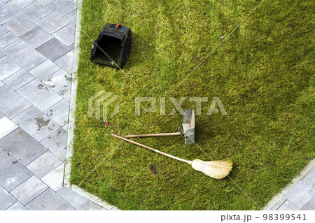 Jug dustpan and a broom on a green grass lawn. Gardening tools. 98399541