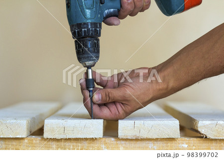 Hand of a worker screws a screw in a wooden board with a cordless screwdriver. Man carpenter at handmade work 98399702