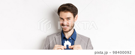 Real estate and insurance concept. Smiling male realtor showing small paper house cutout and looking at camera, selling property, white background Real estate and insurance concept. Smiling male realtor showing small paper house cutout and looking at camera, selling property, white background 98400092