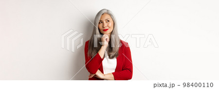 Business concept. Smiling mature lady in red blazer, smiling and looking satisfied while thinking, standing over white background 98400110
