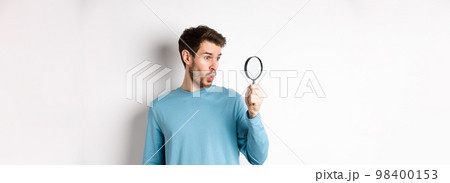 Man got surprised while looking through magnifying glass, saying wow at awesome product, standing over white background 98400153