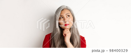 Close up of thoughtful asian business woman looking at upper left corner, thinking or making choice, standing over white background 98400329