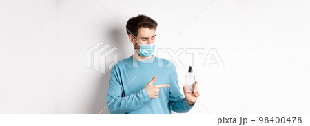 Covid-19, health and quarantine concept. Young man pointing and looking at hand sanitizer bottle, showing good antiseptic, white background 98400478