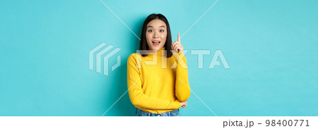 Excited asian woman with short dark hair, pitching an idea, raising finger in eureka gesture and smiling, standing over blue background 98400771