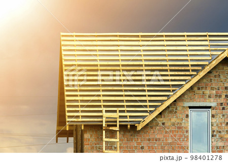 Close-up detail of new brick house top with two narrow plastic attic windows and wooden roof frame under construction on dark blue sky background. Real estate property and professional work concept. 98401278