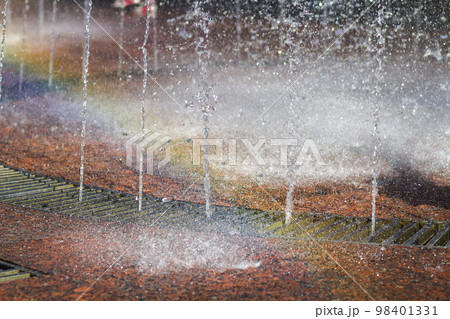 Close up of beautiful city fountain. Splashing upward crystal thin streams of clear cool transparent water, shiny droplets. Multicolored blurred rainbow, recreation area. 98401331