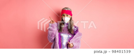 Coronavirus and shopping concept. Worried asian senior woman in stylish outfit and respirator pointing upper right corner, looking unsure at camera, asking advice, pink background Coronavirus and shopping concept. Worried asian senior woman in stylish outfit and respirator pointing upper right corner, looking unsure at camera, asking advice, pink background 98401539