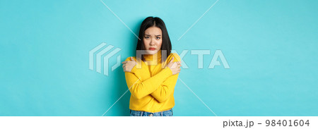Young asian woman feeling like victim, cover body with hands and looking anxious at camera, standing over blue background 98401604