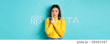 Victim of domestic violance, young asian woman, touching cheek and frowning, being slapped in face, standing over blue background 98402487
