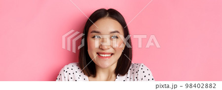 Beauty and lifestyle concept. Headshot of excited asian girl smiling, looking left at promo banner, standing over pink background Beauty and lifestyle concept. Headshot of excited asian girl smiling, looking left at promo banner, standing over pink background 98402882