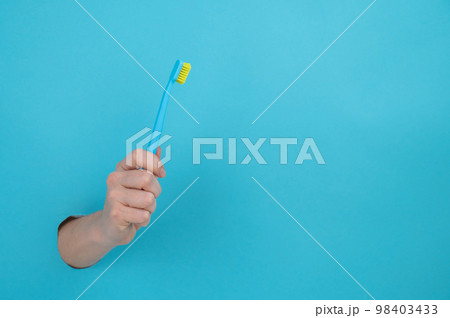 A woman's hand sticks out of a blue paper background and holds a toothbrush. A woman's hand sticks out of a blue paper background and holds a toothbrush. 98403433