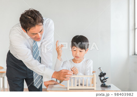 学校の授業で理科の実験・観察・研究・勉強をする小学生の男の子と先生・教師(顕微鏡・試験管・スポイト) 98403982