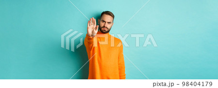 Serious frowning man showing stop gesture, telling no, prohibit and disagree, standing over light blue background 98404179