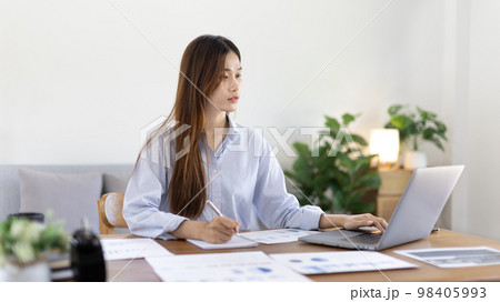 Beautiful young asian woman watching live video or video call of teacher teaching on laptop in her home, Take notes of important conversations and messages during the teacher's teaching. Beautiful young asian woman watching live video or video call of teacher teaching on laptop in her home, Take notes of important conversations and messages during the teacher's teaching. 98405993