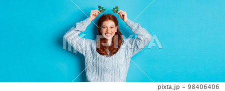 Winter holidays and Christmas sales concept. Beautiful redhead female model celebrating New Year, wearing funny party headband and sweater, smiling at camera 98406406