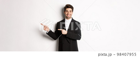 Image of attractive smiling guy dressed for new year party, pointing fingers right and showing advertisement, standing over white background 98407955