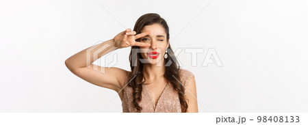 Concept of New Year celebration and winter holidays. Close-up of glamour woman in party dress, red lips, showing peace sign and winking sexy at camera, white background 98408133