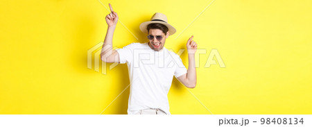 Tourism, travelling and holidays concept. Male tourist enjoying vacation, dancing in straw hat and sunglasses, pointing fingers sideways 98408134