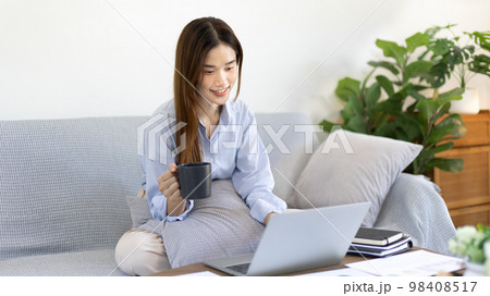 Beautiful Asian woman working on laptop and sipping coffee with smiling face in her home, Creating happiness at work with a smile, Freelancer working at home happily, Work from home. 98408517