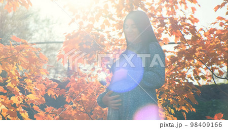 Pregnant woman in sun glare light autumn outdoor. Happy girl with pregnant belly standing in orange fall foliage. Mother expecting child. Maternity, motherhood care in natural park. Tranquil pregnancy 98409166
