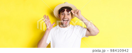 Concept of tourism and holidays. Excited man tourist take-off sunglasses and looking amazed at promo offer, standing over yellow background Concept of tourism and holidays. Excited man tourist take-off sunglasses and looking amazed at promo offer, standing over yellow background 98410942