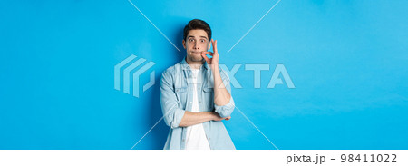 Adult man zipping mouth, promise keep secret, making a seal on lips and standing over blue background Adult man zipping mouth, promise keep secret, making a seal on lips and standing over blue background 98411022