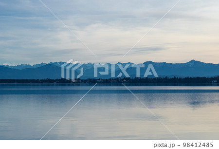 Starnberger See, Germany - December 30th 2022: Flat water surface of the lake in front of the alpine ridge Starnberger See, Germany - December 30th 2022: Flat water surface of the lake in front of the alpine ridge 98412485