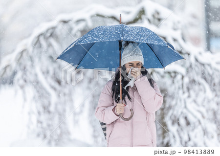 Woman clears her running nose standing on the street under an umbrella on a snowy day 98413889