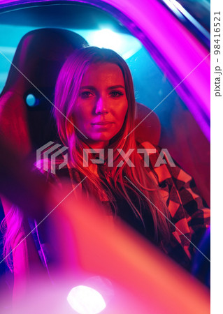 Portrait of beautiful young woman driving car at night in neon light. 98416521